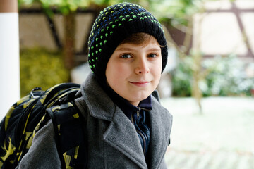 Portrait of preteen kid boy outdoors. Handsome child boy in coat and hat in winter. Schoolchild on the way to school with backpack satchel during snow