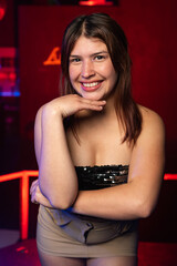 Fototapeta premium young caucasian woman posing from the front and smiling on a background of red lights. night party concept.