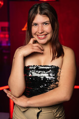 Fototapeta premium young latin woman posing from the front and smiling on a background of red lights. night party concept.