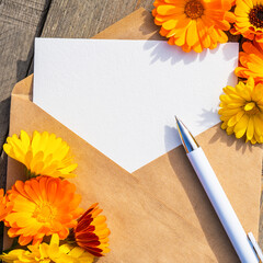 An empty paper postcard, an envelope and a calendula flower on a wooden background, a postcard layout with a place to copy, a template, a flat layout. A place to copy. Selective focus.