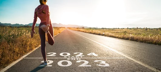 Foto op Plexiglas New year 2024 or start straight concept.word 2024 written on the asphalt road and athlete woman runner stretching leg preparing for new year at sunset.Concept of challenge or career path and change. © Yingyaipumi