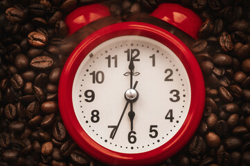 Red alarm clock on a background of coffee beans. A close-up of the alarm clock shows six o'clock in...
