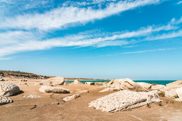 Fototapeta na wymiar Fragments of ancient rocks on sandy beach. Sea shallowing