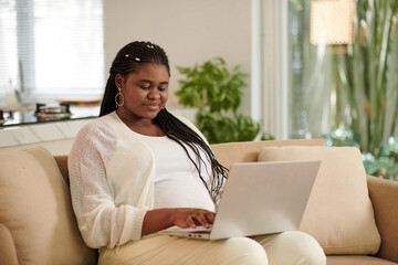 Positive Black pregnant woman working on laptop at home