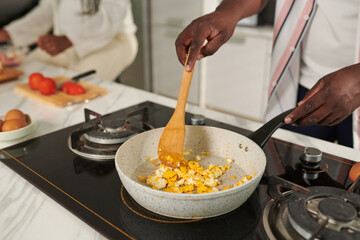Closeup image of man cooking scrambled eggs for family breakfast