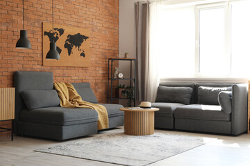 Obraz premium Modern living room interior with gray modular sofa, wooden coffee table, brick wall, and bright window