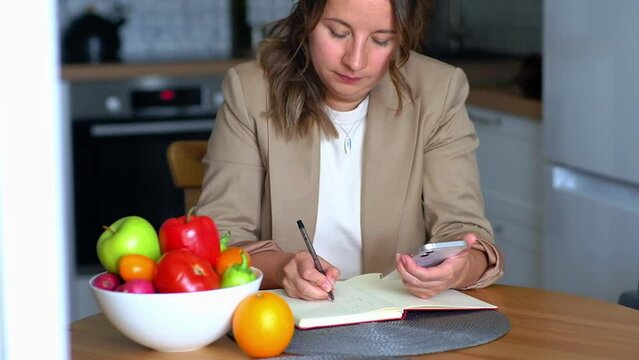 A female nutritionist sits at her desk and consults a patient over the phone and draws up a nutrition plan