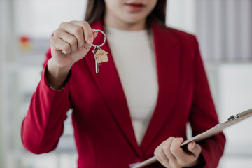 Smiling female realtor selling an apartment, offering it to a client, showing at camera, holding...