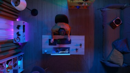 Top view of man in casual clothing sitting at the desk playing, streaming game on computer online.