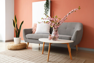 Interior of stylish living room with grey sofa and blooming sakura branches on coffee table