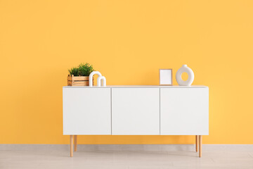 Modern chest of drawers with houseplant and decor near orange wall in room