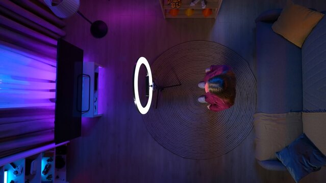 Top view of girl in the living room in casual clothing standing in front of smartphone camera and ring light.