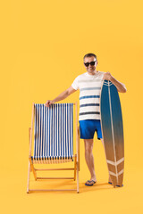 Mature man with surfboard and deck chair on yellow background