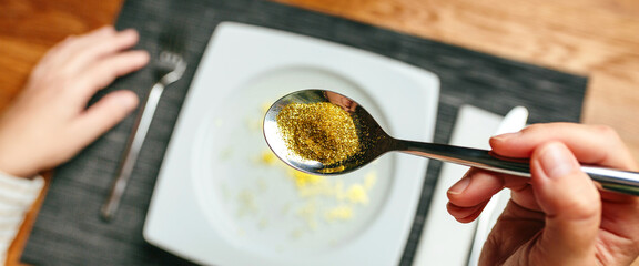 Banner of unrecognizable woman hand holding a spoon full of golden glitter composed of plastics harmful to humans and environment. Concept about risks of eating food contaminated with microplastics.