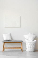 Fototapeta na wymiar Grey bench and basket with pillows near white wall