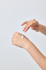 Asian woman's hand applying white cosmetic formulation on the back of her hand.