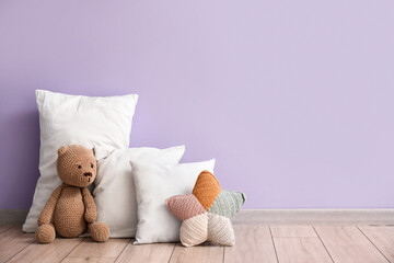 White pillows with teddy bear near lilac wall