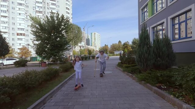Child girl teaches an old man to ride a skateboard. They are training to ride a skateboard on the street. Grandpa is riding a skateboard.