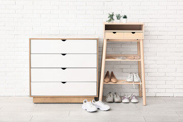 Shoe rack with stylish shoes and orthopedic insoles near light brick wall in room