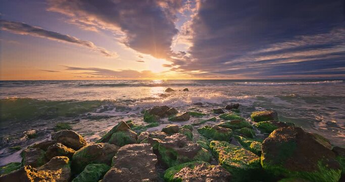 Sea sunrise over the waves and beach, ocean rocky coast at sunset and crashing waves on frontline stones
