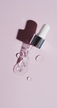 Vertical video of make up pipette and drops of serum with copy space on pink background