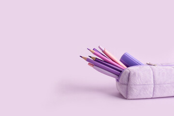 Pencil case with school stationery on purple background