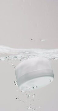 Vertical video of beauty product tub falling in water with copy space on white background