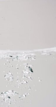 Vertical video of beauty product bottle falling in water with copy space on white background