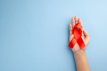 AIDS awareness and healthcare concept - Female hands holding a red ribbon with a stethoscope on a...