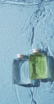 Vertical video of beauty product bottles in water with copy space on blue background