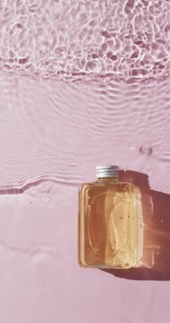 Vertical video of beauty product bottle in water with copy space on pink background