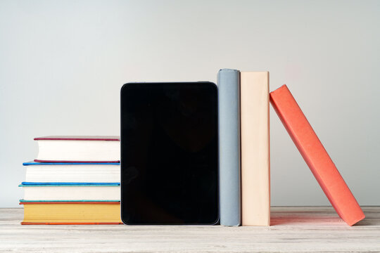 Digital tablet with a stack of books on gray background