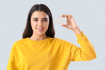 Young woman with birth control pills on light background