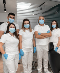 Professional doctors stand together looking at the camera. A team of medics wearing protective medical blue masks and gloves. Dentists recommend