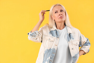 Thoughtful mature woman with pen on yellow background