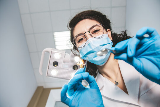 Creative portrait of female dentist examining patient on dentist chair, view from patient's side.