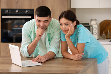 Happy young couple with laptop in kitchen