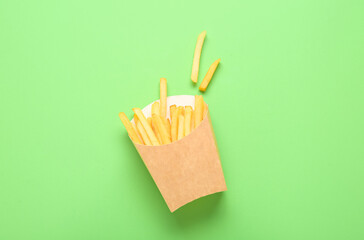 Paper box with delicious french fries on green background
