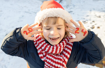 smiling cheerful child in Santa hat and striped red scarf closed eyes and makes wish. numbers of...