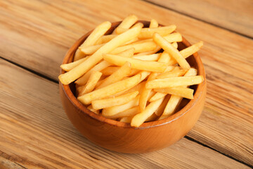 Bowl with tasty french fries on brown wooden background