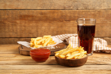 Bowl with tasty french fries, cola and bowl of ketchup on brown wooden background