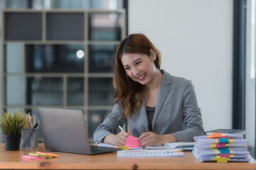 Portrait of smiling Asian businesswoman working on laptop at workplace in modern office.
