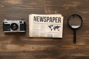 Morning newspaper, magnifying glass and photo camera on wooden background