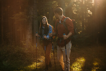 A multicultural pair with backpacks and walking sticks discover the beauty of the outdoors, their beaming smiles mirroring their excitement for the journey ahead