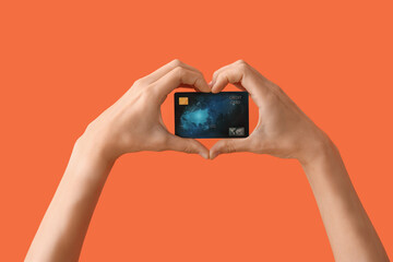 Woman with credit card making heart gesture on orange background