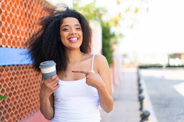 Young African American woman holding a take away coffee at outdoors and pointing it