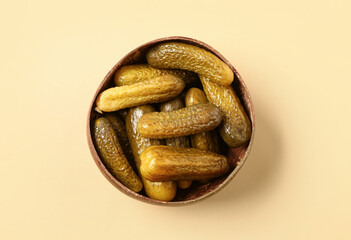 Wooden bowl with tasty pickled cucumbers on orange background