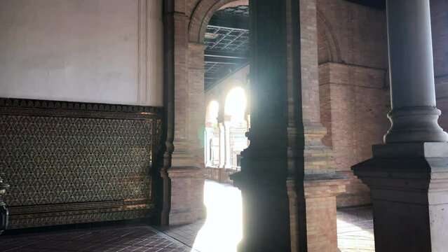 Semi-circular interior shot of Plaza de Espana in Seville, Spain. Sunlit brick and stone pillars with patterned wall.