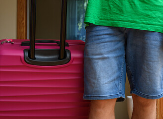 Mężczyzna trzyma spakowaną różową walizkę podróżną - obrazy, fototapety, plakaty