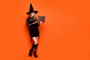 Full length photo of sweet cute lady wear black wizard costume cap chatting modern gadget empty space isolated orange color background